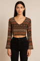 Woman wearing a patterned long-sleeve top and black pants on a beige background