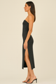 Woman wearing a strapless black dress with a slit on a beige background