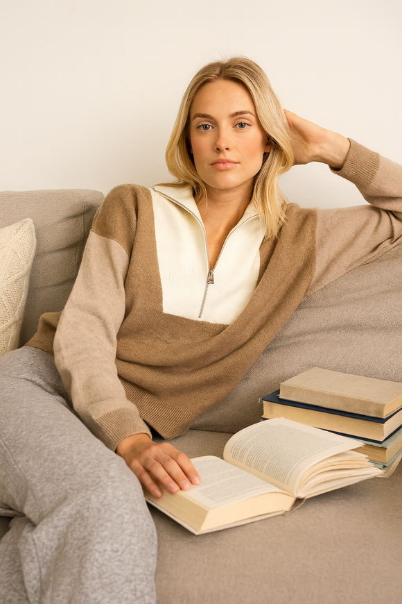 Woman sitting on a couch with an open book, wearing a beige and white sweater.