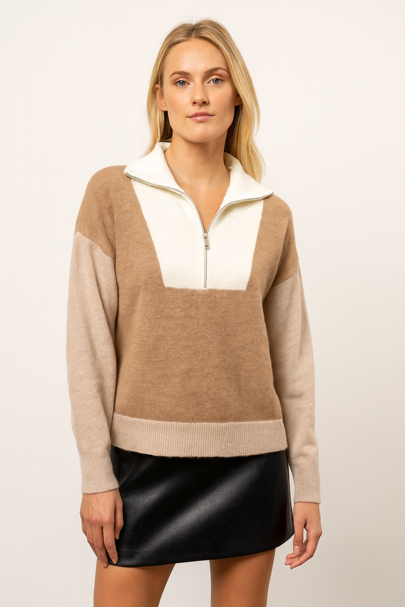 Woman wearing a beige and white color-blocked sweater with a black skirt on a plain background