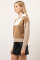 Woman wearing a brown and beige color-blocked sweater with a white collar on a light background