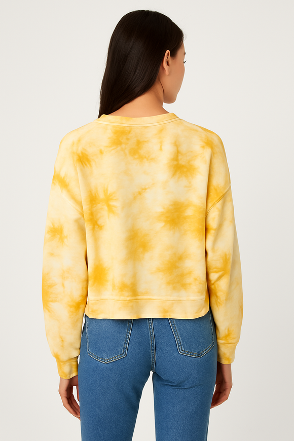Person wearing a yellow tie-dye sweatshirt and blue jeans on a white background