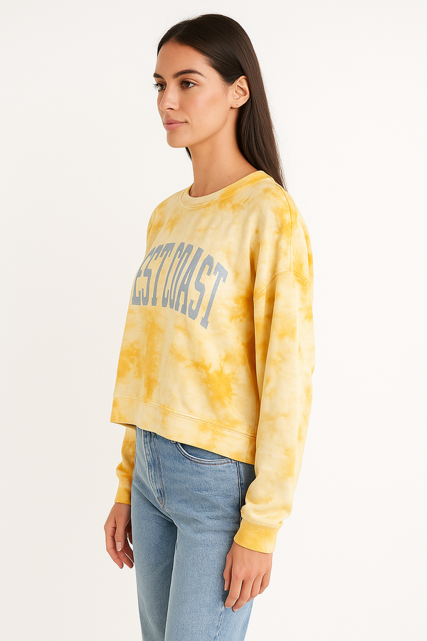 Woman wearing a yellow tie-dye sweatshirt with 'West Coast' text on a white background