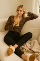 Woman sitting on a couch holding a drink, wearing a patterned top and black pants.