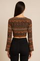 Woman wearing a patterned long-sleeve top and black pants on a beige background