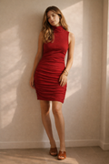 Woman wearing a red dress standing against a neutral wall.