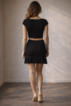 Woman wearing a black outfit with a crop top and skirt against a neutral background