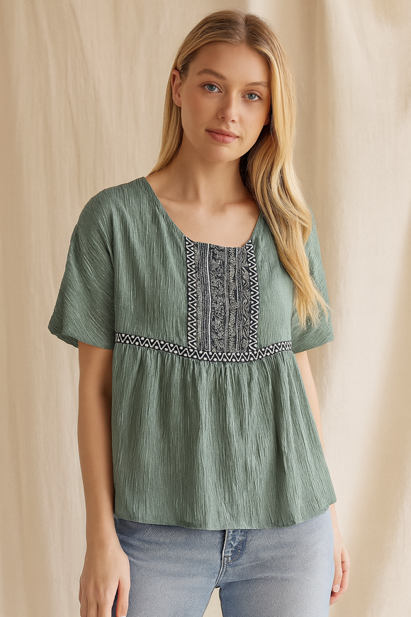 Woman wearing a green blouse with embroidery details against a beige background