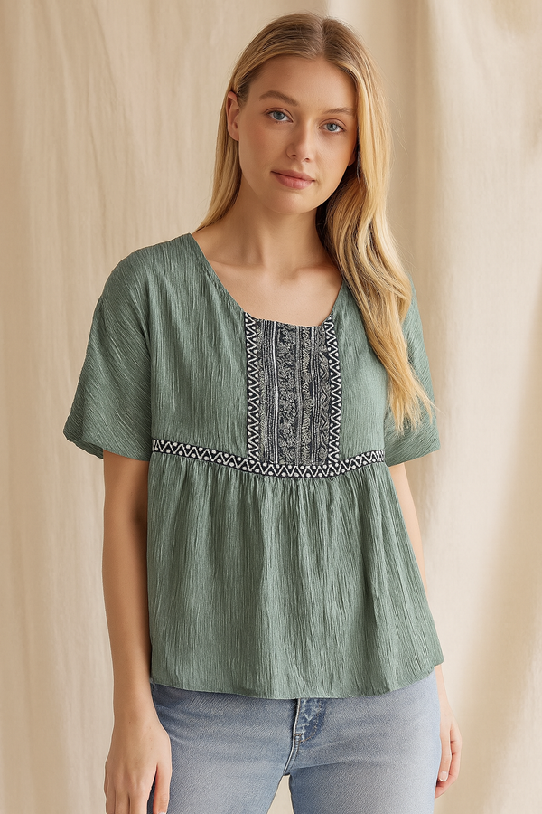 Woman wearing a green blouse with embroidery details against a beige background