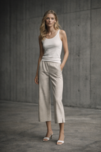 Woman wearing a white tank top and beige checkered capri pants against a gray concrete wall.