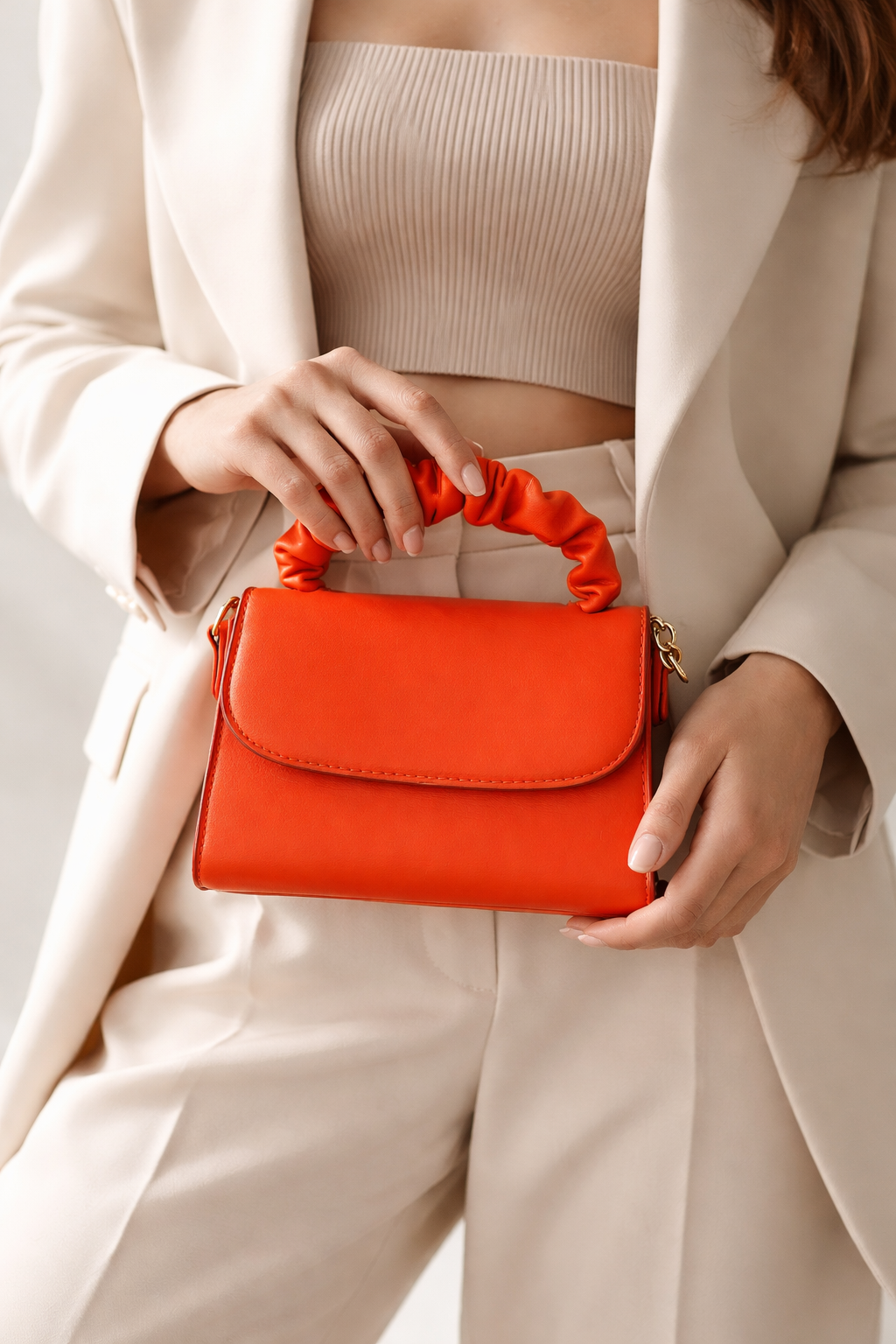 Person holding a orange handbag with a neutral outfit