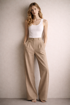 Woman wearing a white tank top and beige pants against a plain background