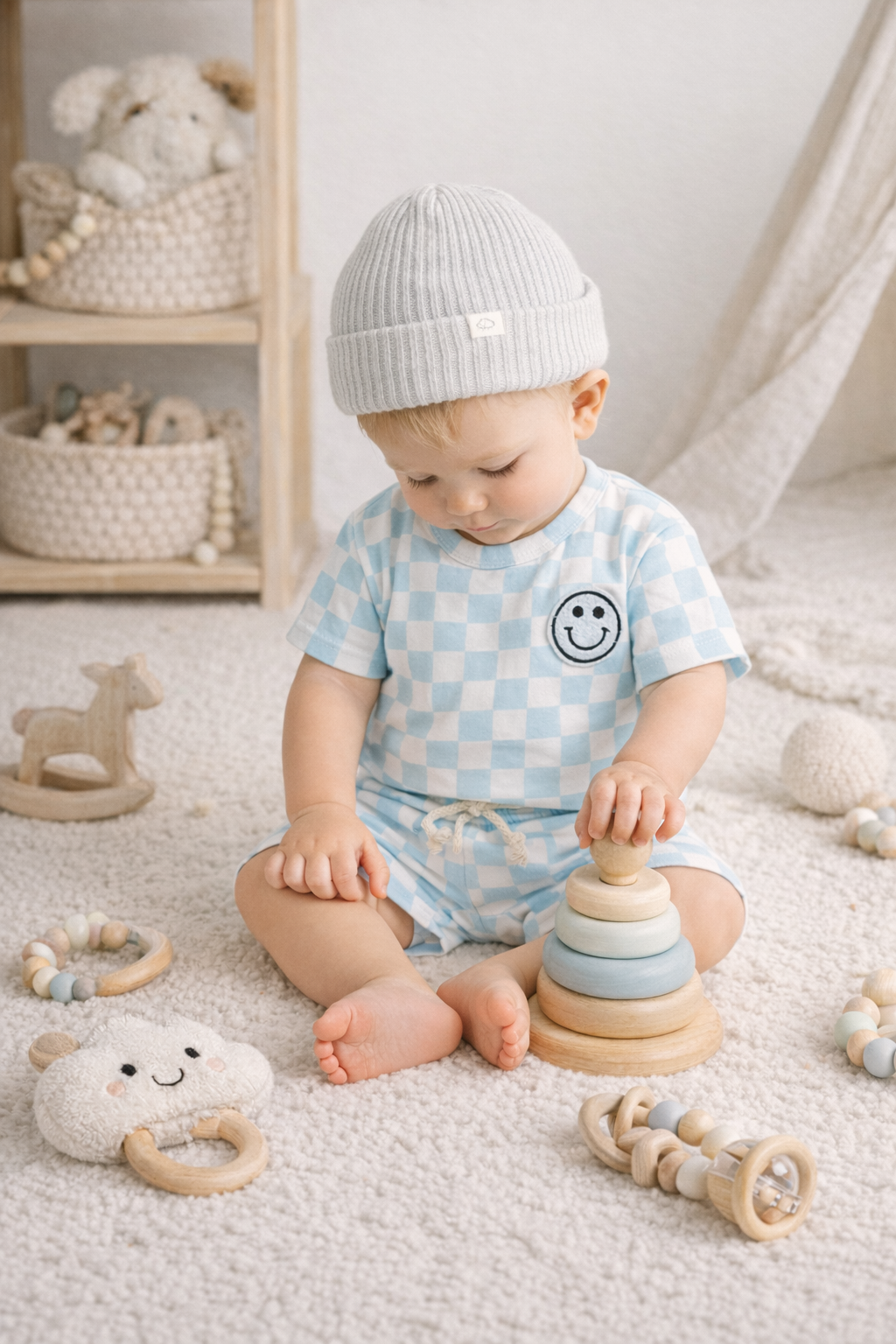 Baby playing with wooden toys on a soft surface wearing a gingham short set with happy face