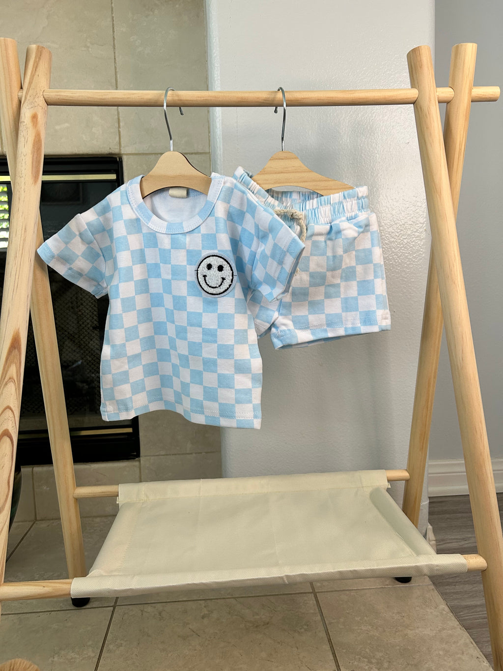 Blue checkered baby outfit with a smiley face design on a wooden rack.