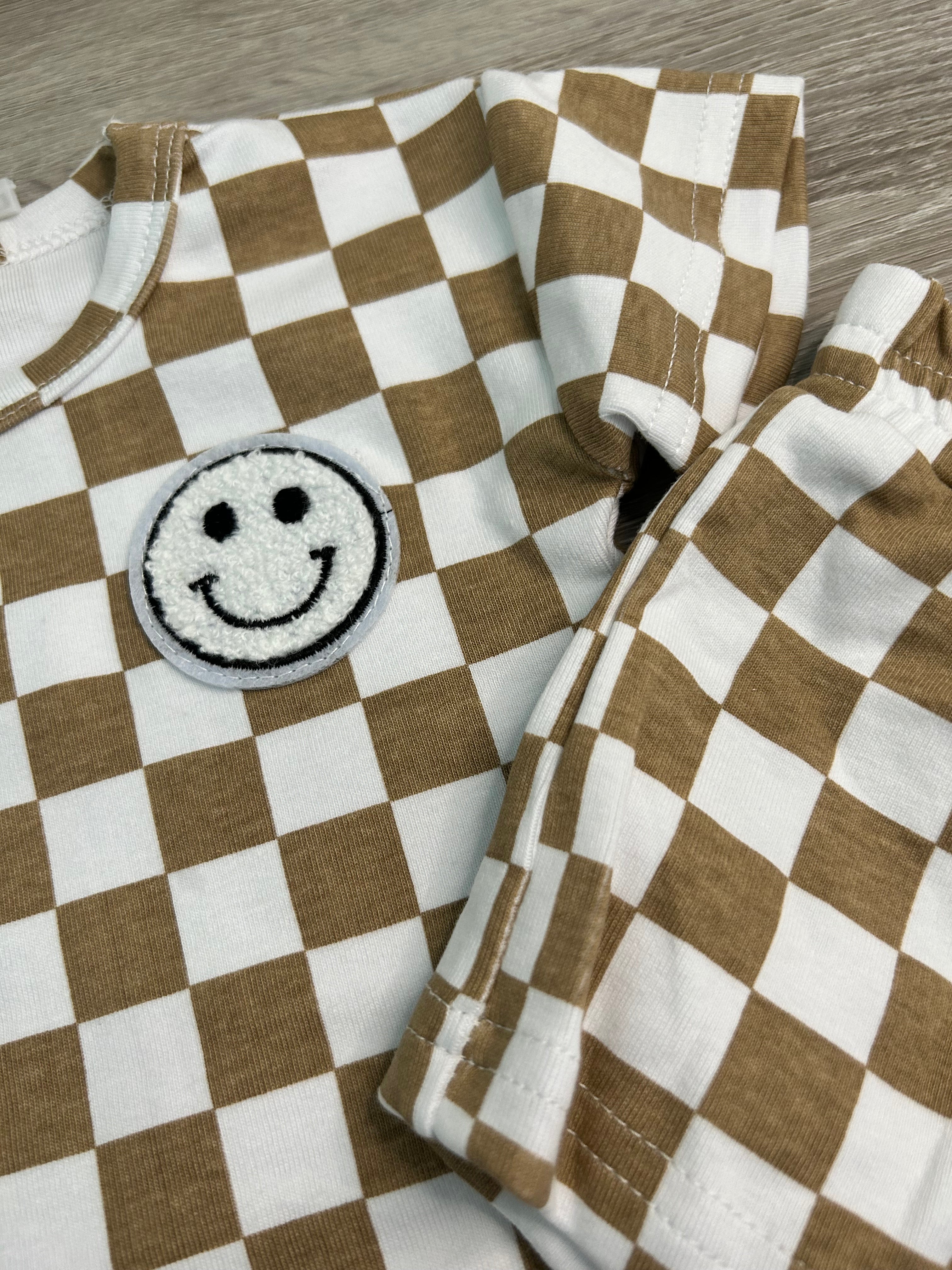 Brown and white checkered fabric with a smiley face patch on a wooden surface