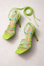 Pair of green strappy high-heeled shoes on a light gray background