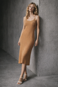 Woman wearing a mustard yellow dress against a gray concrete wall.