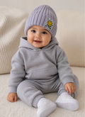 Baby wearing a gray hoodie and pants set with a matching hat, sitting on a beige surface.