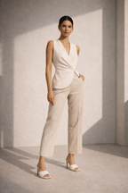 Woman wearing a white sleeveless top and beige pants against a light gray wall.