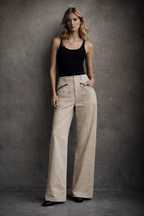 Woman wearing a black tank top and beige pants against a gray background
