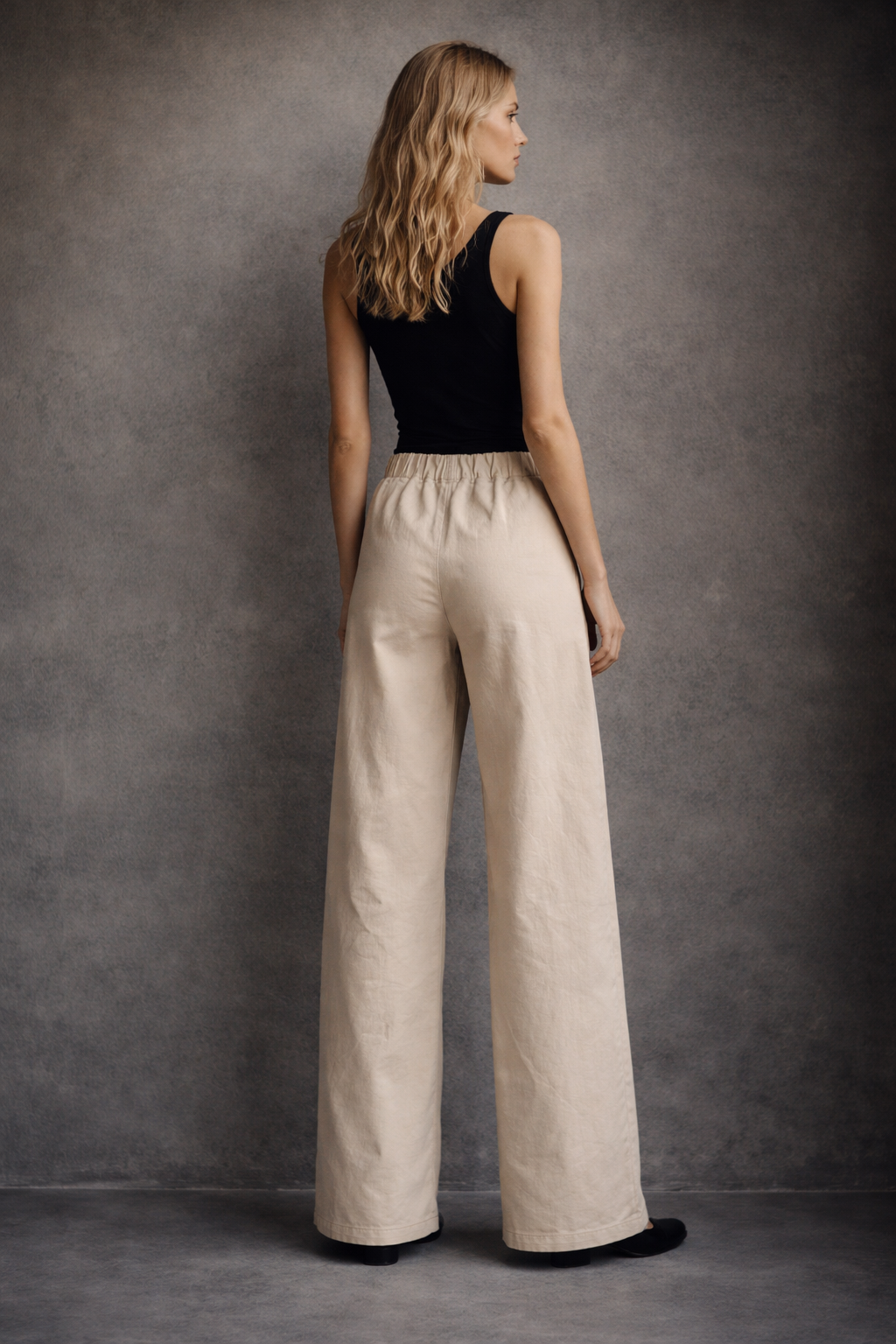 Woman wearing beige wide-leg pants and a black top against a gray background