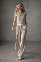Woman wearing a beige sleeveless top and wide-leg pants against a gray background