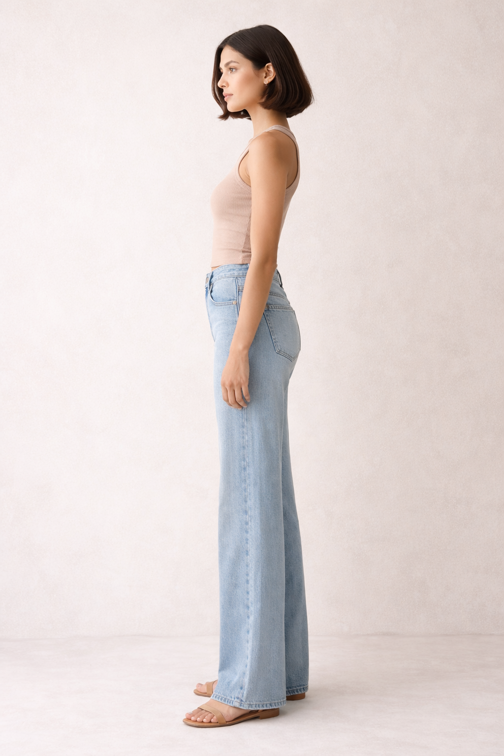 Woman wearing light blue jeans and a beige top on a plain background