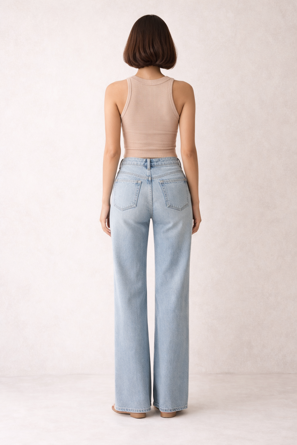 Person wearing light blue jeans and a beige tank top on a white background