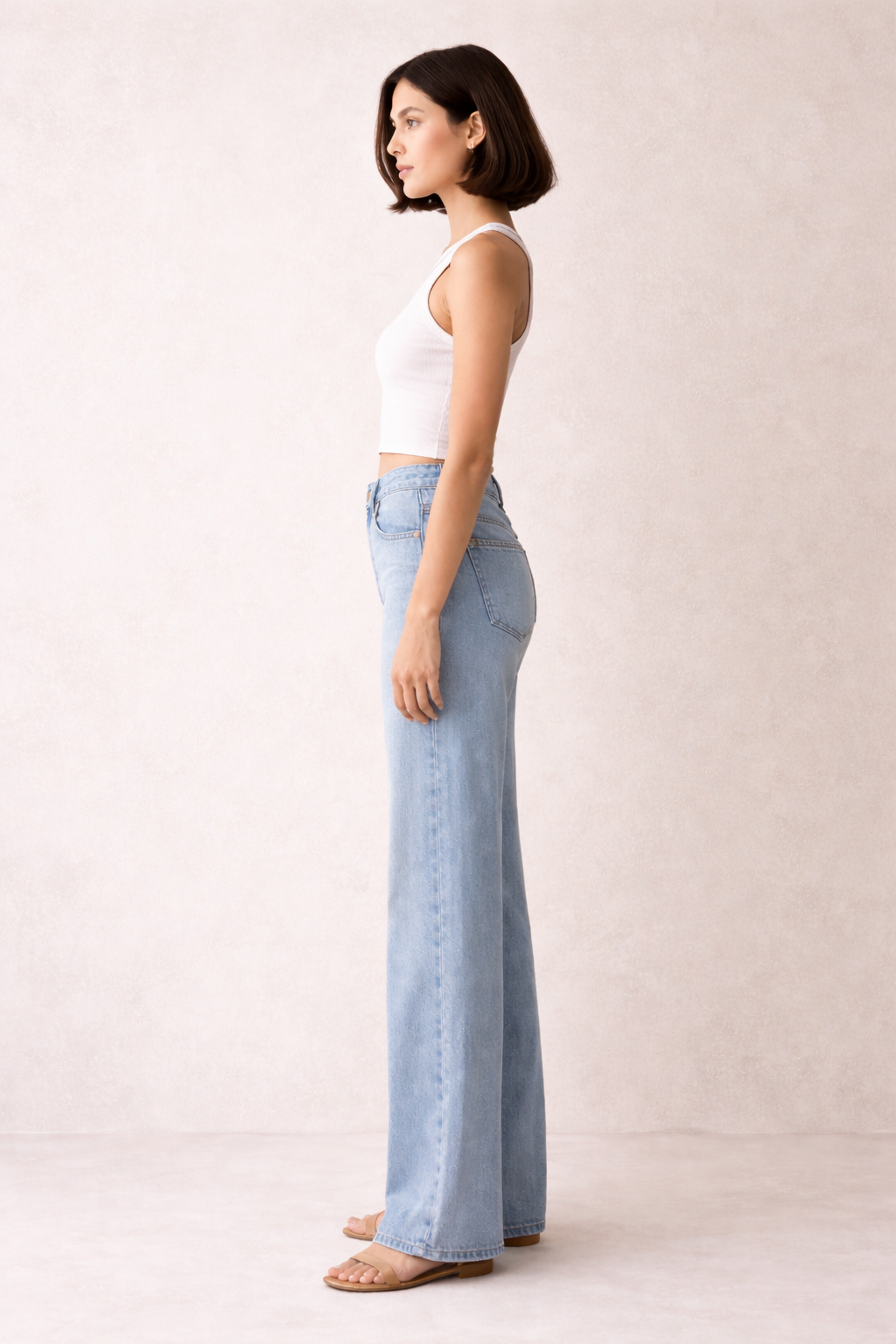 Woman wearing light blue jeans and a white top against a plain background