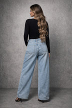 Woman wearing light blue jeans and a black top against a gray background