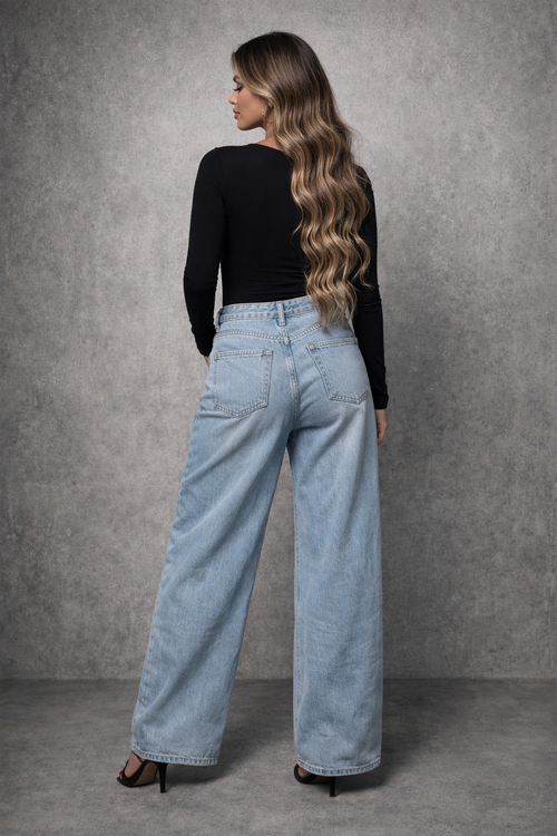 Woman wearing light blue jeans and a black top against a gray background