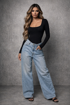 Woman wearing a black long-sleeve top and light blue jeans against a gray background