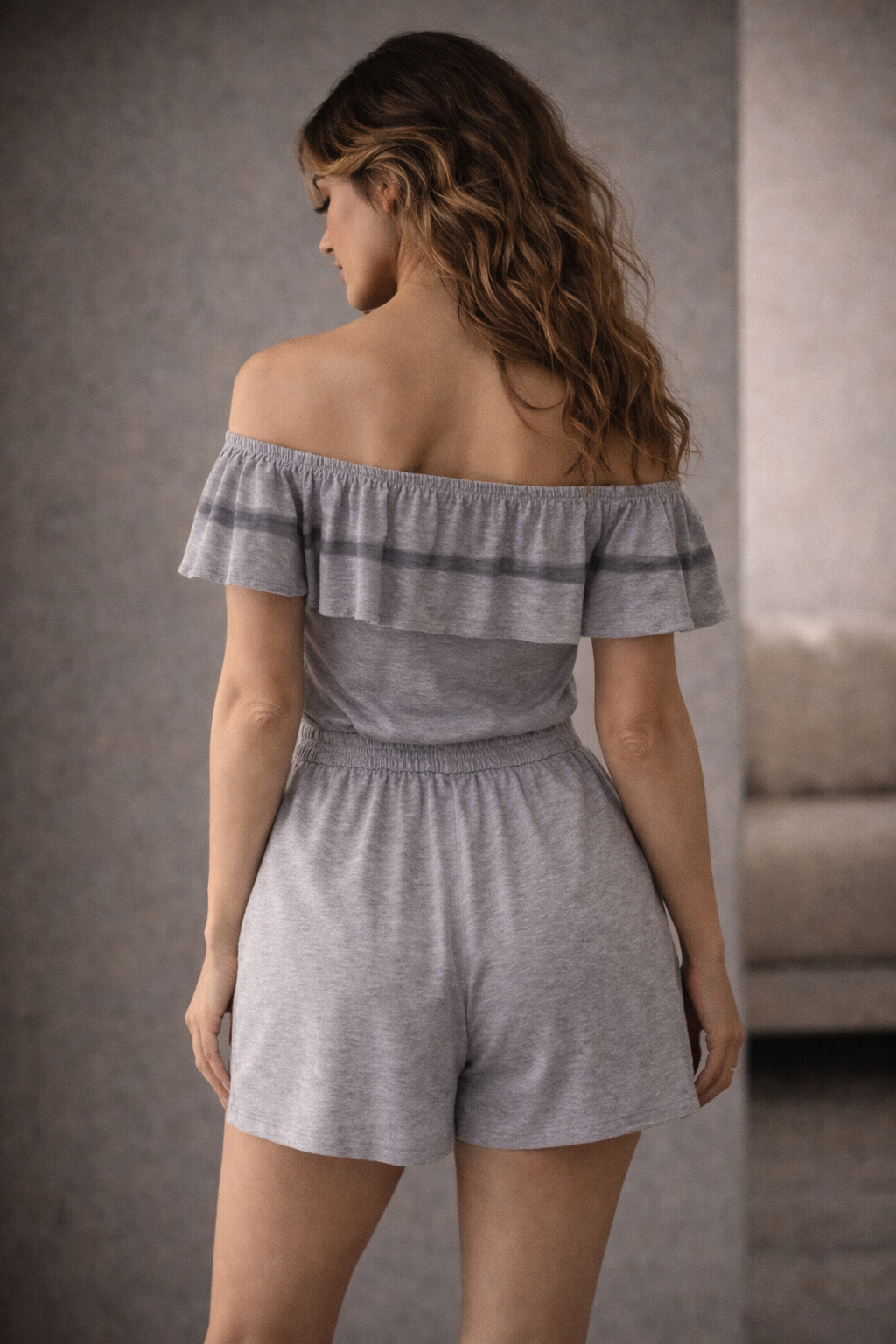 Woman wearing a gray off-shoulder romper against a neutral background
