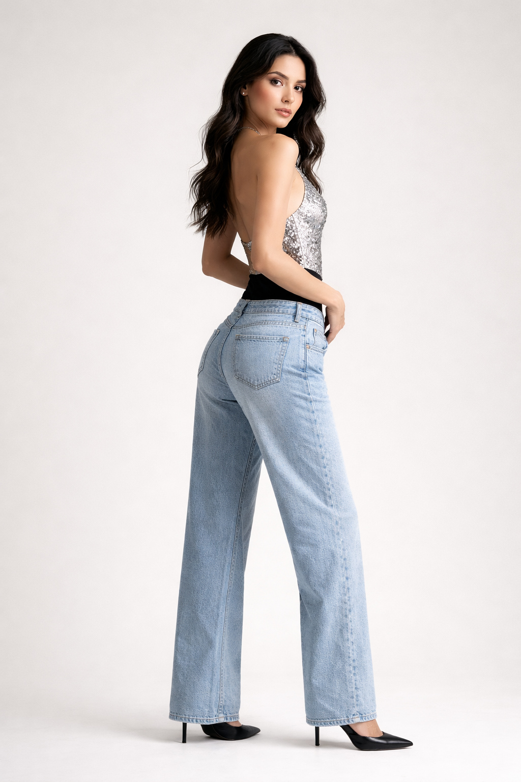 Woman wearing light blue jeans and a black top with sequins on a white background